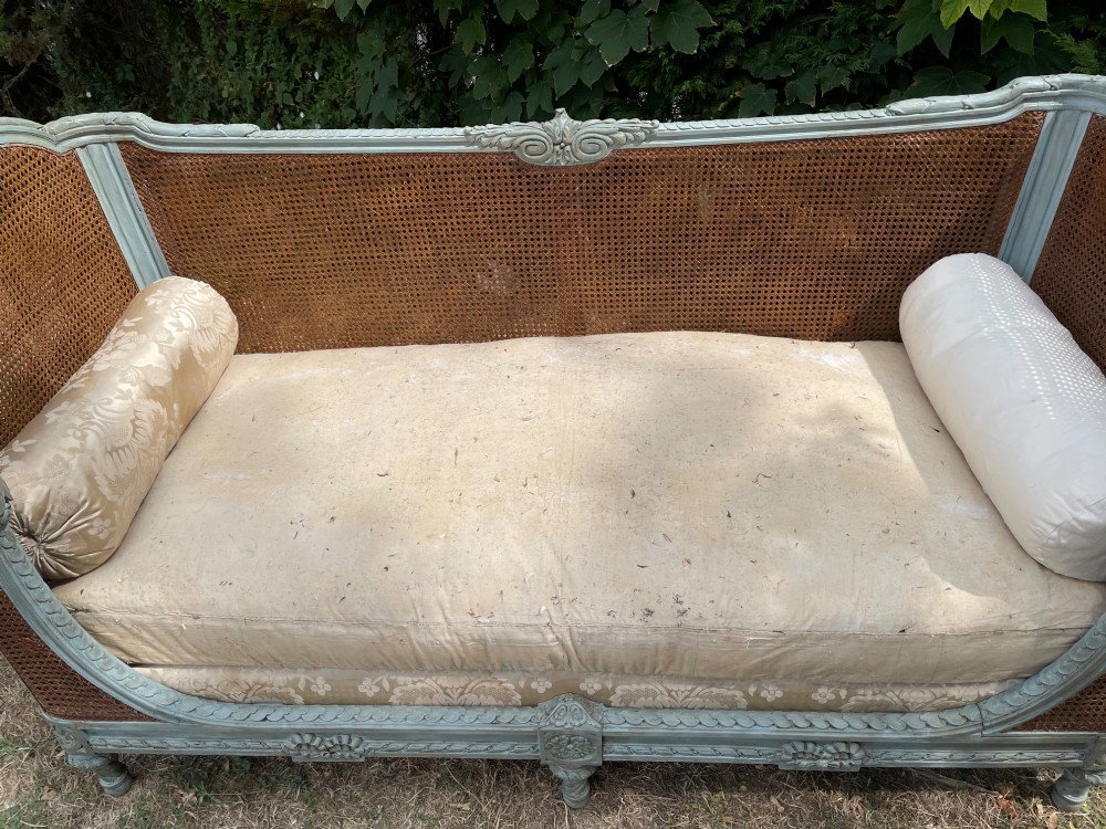 A French Louis XVI style daybed featuring a grey-painted curved timber frame with woven cane panels, fitted with a cream linen mattress cushion and two bolster pillows. View V