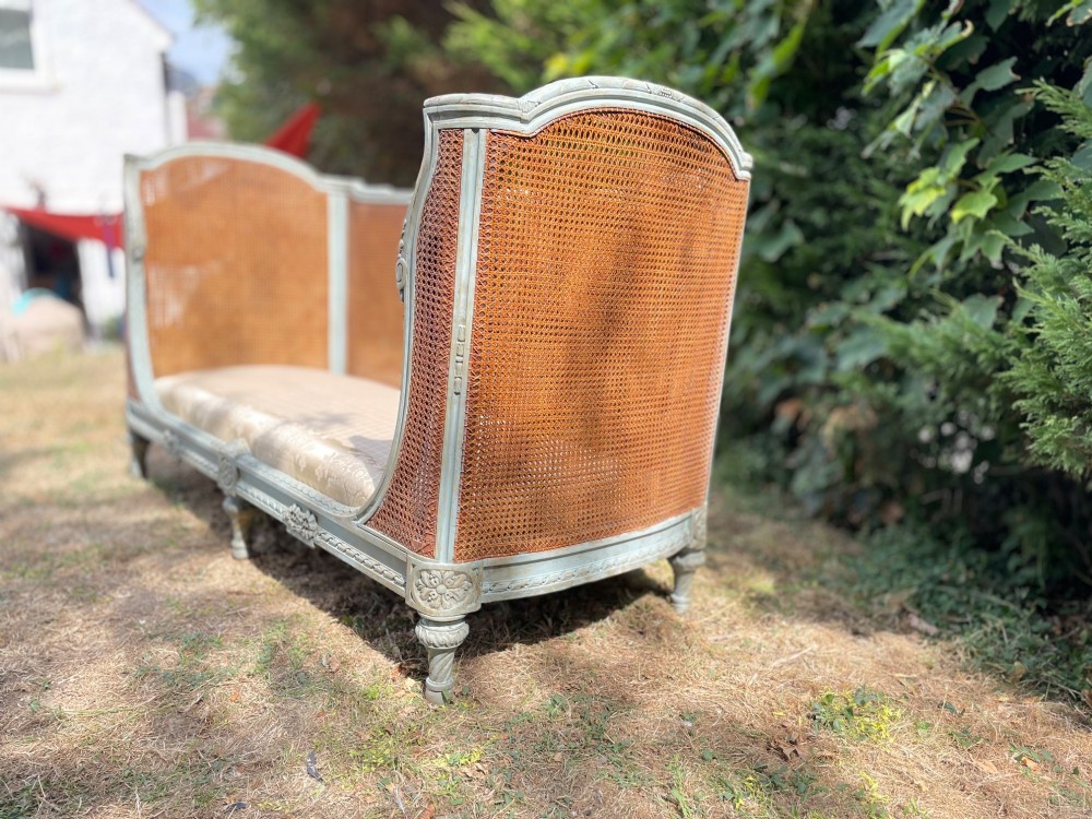 A French Louis XVI style daybed featuring a grey-painted curved timber frame with woven cane panels, fitted with a cream linen mattress cushion and two bolster pillows. View XIV