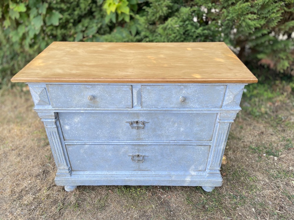 A French Gustavian style chest of drawers featuring a natural wood top, pale blue distressed paint finish, fluted corner pilasters, carved diamond-point details, and metal drop handles.
