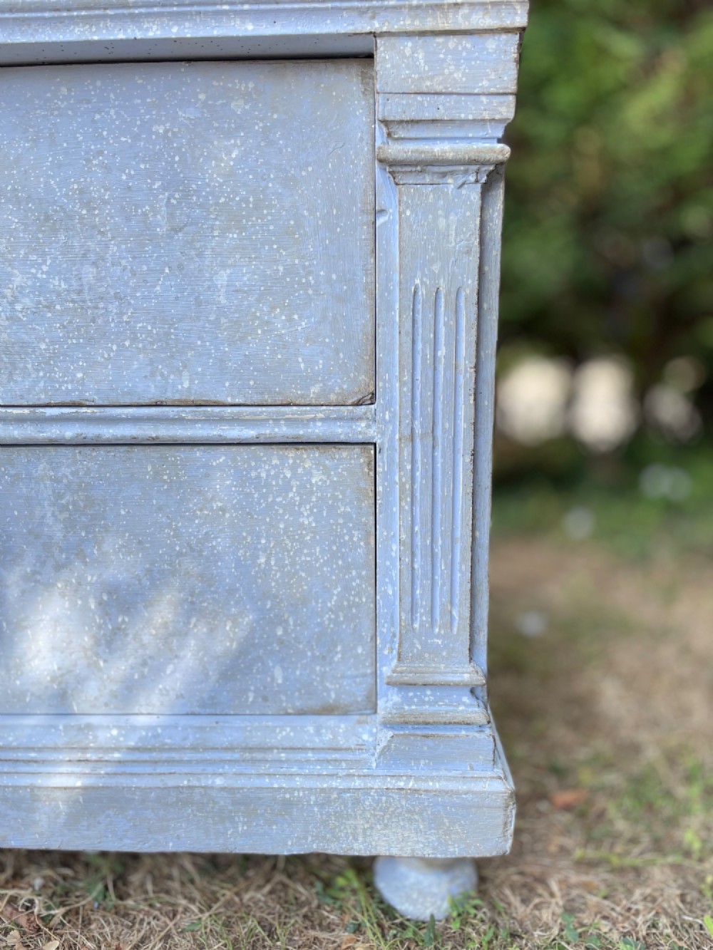 A French Gustavian style chest of drawers featuring a natural wood top, pale blue distressed paint finish, fluted corner pilasters, carved diamond-point details, and metal drop handles. View III