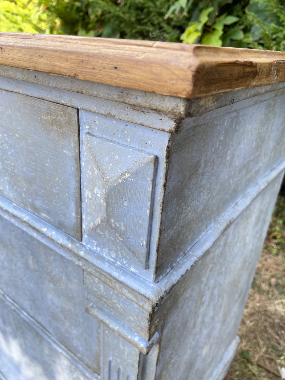 A French Gustavian style chest of drawers featuring a natural wood top, pale blue distressed paint finish, fluted corner pilasters, carved diamond-point details, and metal drop handles. View V