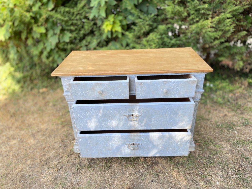 A French Gustavian style chest of drawers featuring a natural wood top, pale blue distressed paint finish, fluted corner pilasters, carved diamond-point details, and metal drop handles. View X