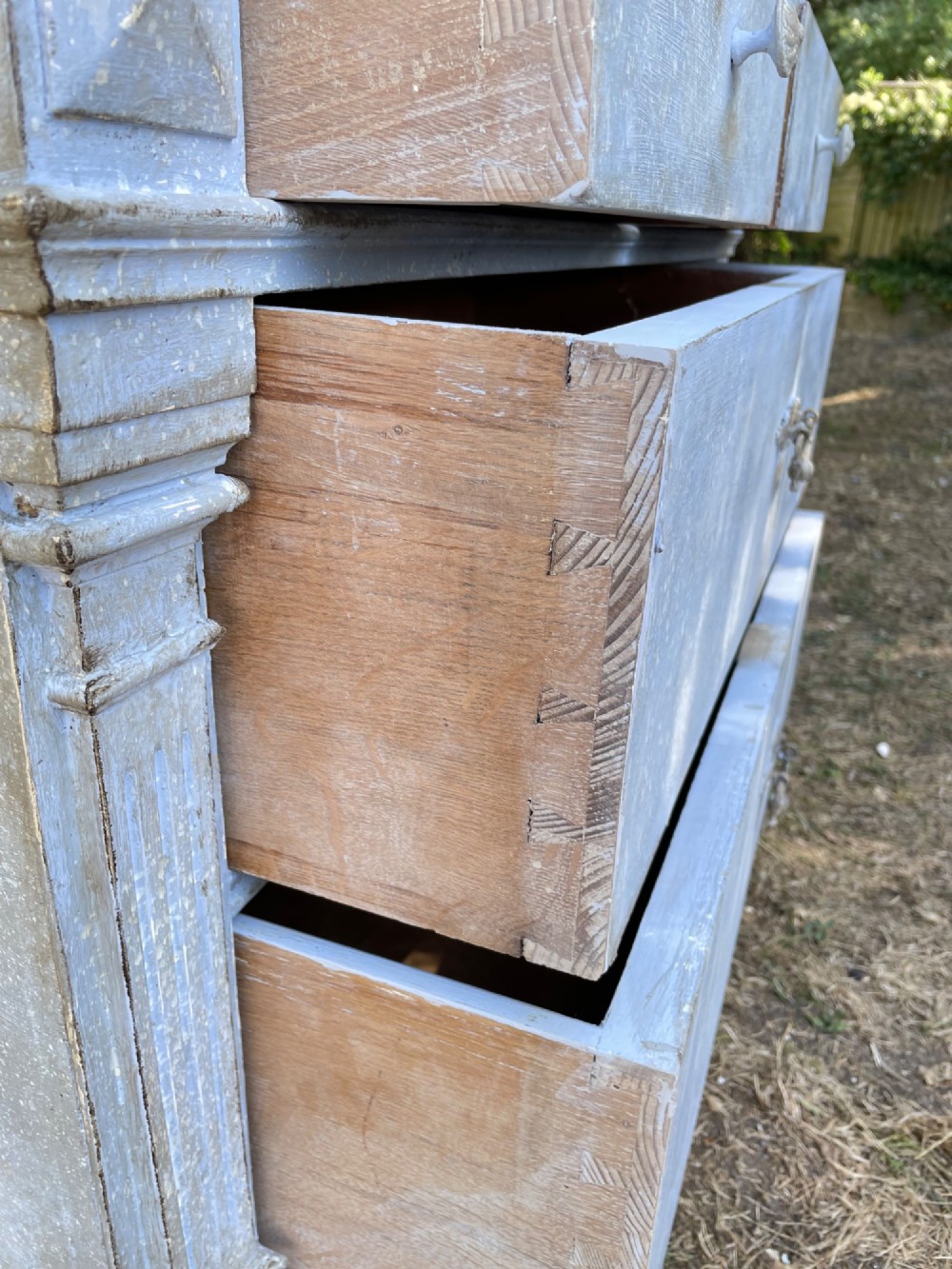 A French Gustavian style chest of drawers featuring a natural wood top, pale blue distressed paint finish, fluted corner pilasters, carved diamond-point details, and metal drop handles. View XII