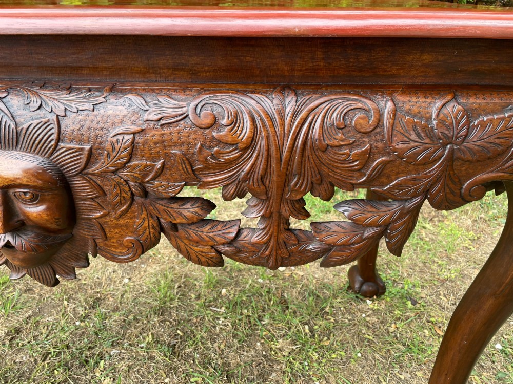 An Edwardian George II style mahogany serving table with an intricately carved apron featuring a central mask motif, raised on cabriole legs with claw and ball feet. View VIII