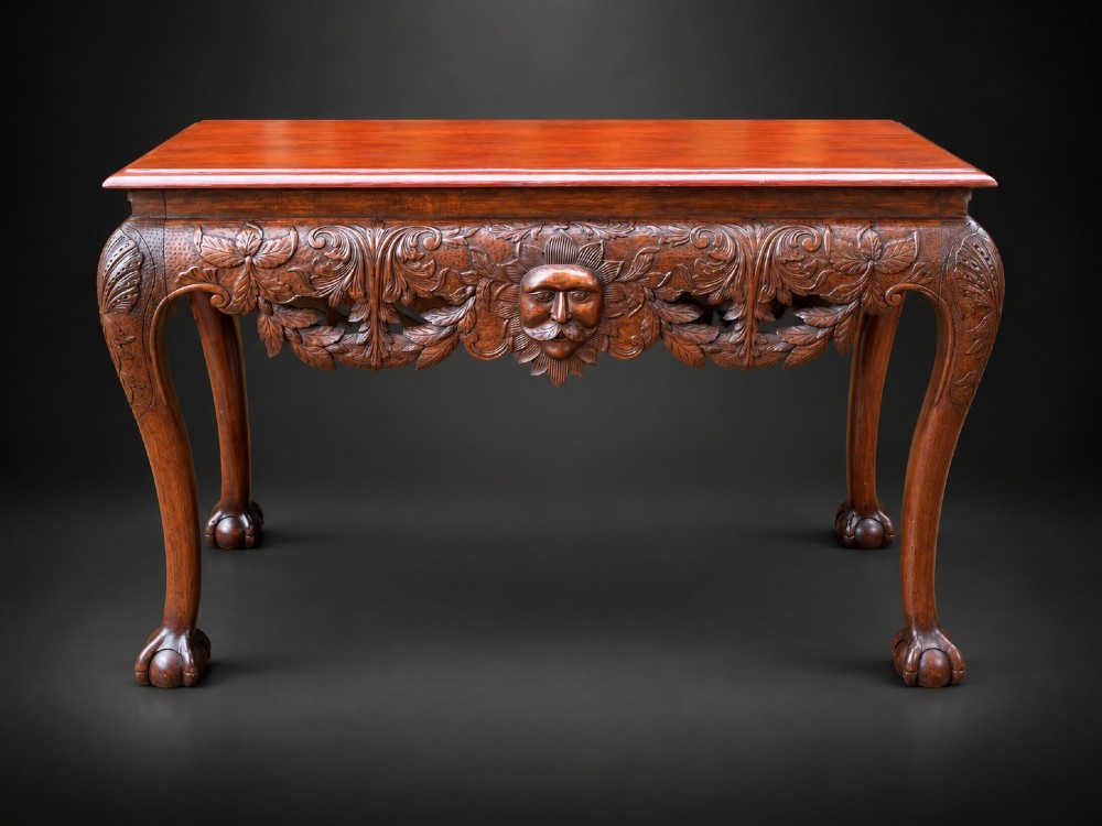 An Edwardian George II style mahogany serving table with an intricately carved apron featuring a central mask motif, raised on cabriole legs with claw and ball feet.