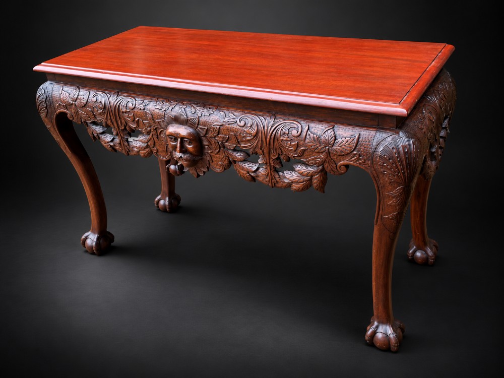An Edwardian George II style mahogany serving table with an intricately carved apron featuring a central mask motif, raised on cabriole legs with claw and ball feet. View XII