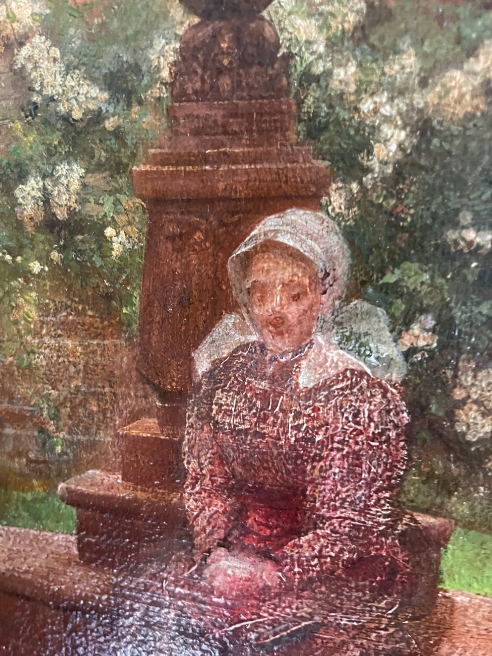 An antique oil painting depicting a woman seated in a walled garden surrounded by trees and a country house, set in an ornate gilded frame. View VII
