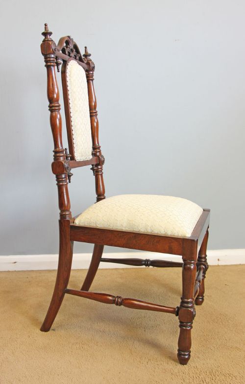 fig 1. An antique Victorian childs dark wood side chair featuring turned legs, decorative finials, carved cresting, and cream upholstery on the seat and back pad.