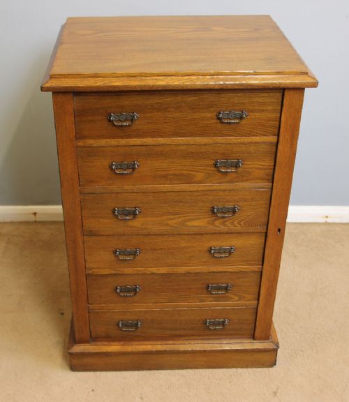 fig 1. A Victorian ash Wellington chest of drawers with six drawers, brass drop handles, and a hinged side locking bar set on a plinth base.
