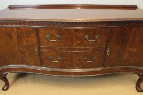 fig 1. An antique dark mahogany serpentine sideboard featuring central drawers, flanking cupboard doors, brass drop handles, carved frieze moulding, and cabriole legs.