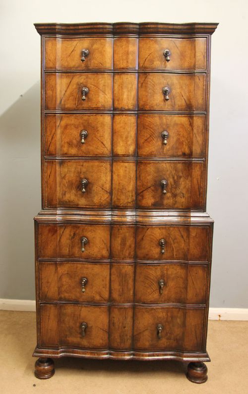 fig 1. An antique figured walnut chest on chest featuring a serpentine shaped front, brass drop handles, and turned bun feet.