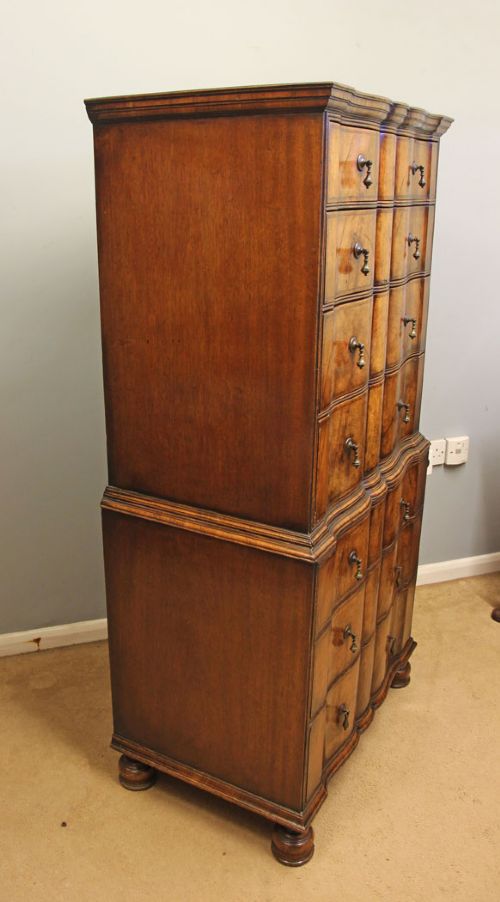 An antique figured walnut chest on chest featuring a serpentine shaped front, brass drop handles, and turned bun feet. View III