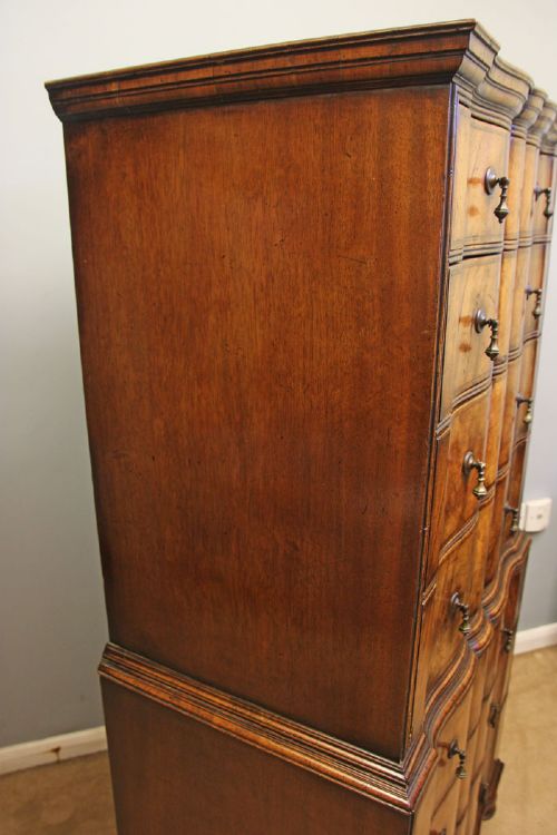An antique figured walnut chest on chest featuring a serpentine shaped front, brass drop handles, and turned bun feet. View IV