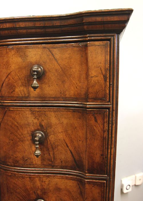 An antique figured walnut chest on chest featuring a serpentine shaped front, brass drop handles, and turned bun feet. View XI