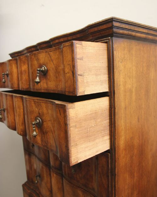 An antique figured walnut chest on chest featuring a serpentine shaped front, brass drop handles, and turned bun feet. View XII