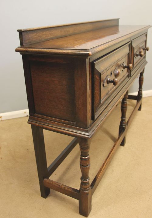 An antique dark oak side table with two geometric-panelled drawers, turned legs, a low stretcher base, and a raised backboard. View IX