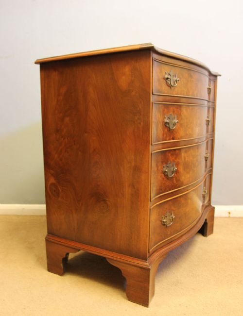 A burr walnut chest of drawers featuring four graduated drawers with a serpentine curved front, decorative brass handles, and resting on bracket feet. View III