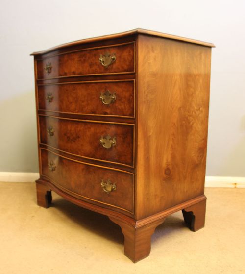 A burr walnut chest of drawers featuring four graduated drawers with a serpentine curved front, decorative brass handles, and resting on bracket feet. View VII