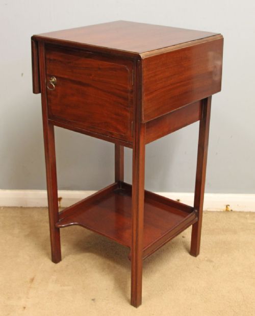 An antique mahogany bedside cabinet featuring two drop-leaf sides, a single door with a brass ring pull handle, straight legs, and an undertier shelf. View II