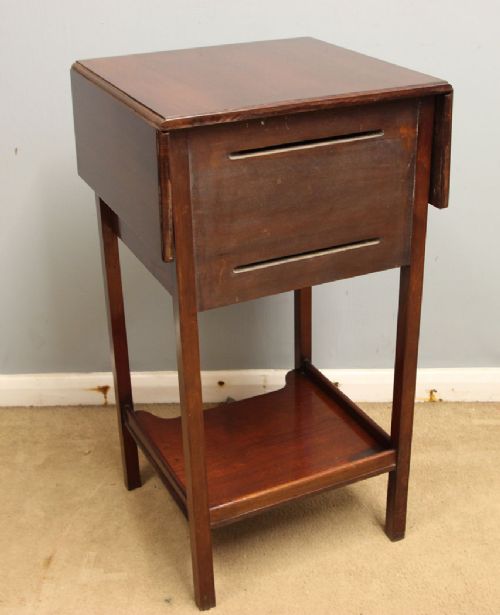 An antique mahogany bedside cabinet featuring two drop-leaf sides, a single door with a brass ring pull handle, straight legs, and an undertier shelf. View VII