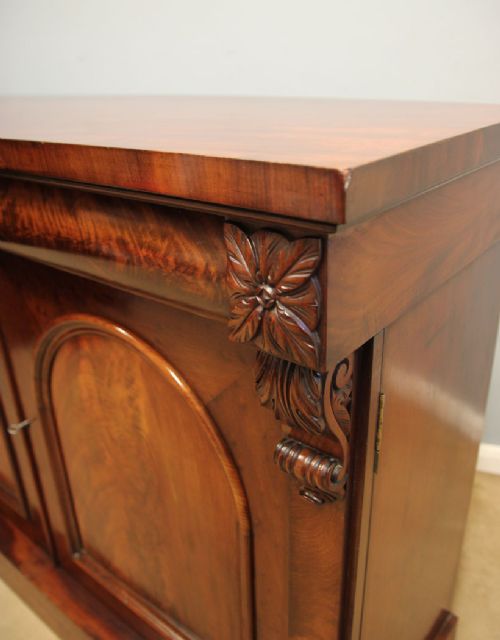 An antique Victorian flame mahogany chiffonier sideboard with two arched panel doors, carved corbels, and a plinth base. View III