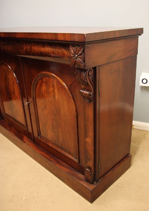 An antique Victorian flame mahogany chiffonier sideboard with two arched panel doors, carved corbels, and a plinth base. View IV