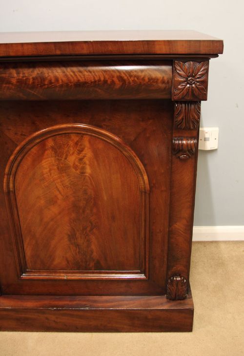 An antique Victorian flame mahogany chiffonier sideboard with two arched panel doors, carved corbels, and a plinth base. View VI