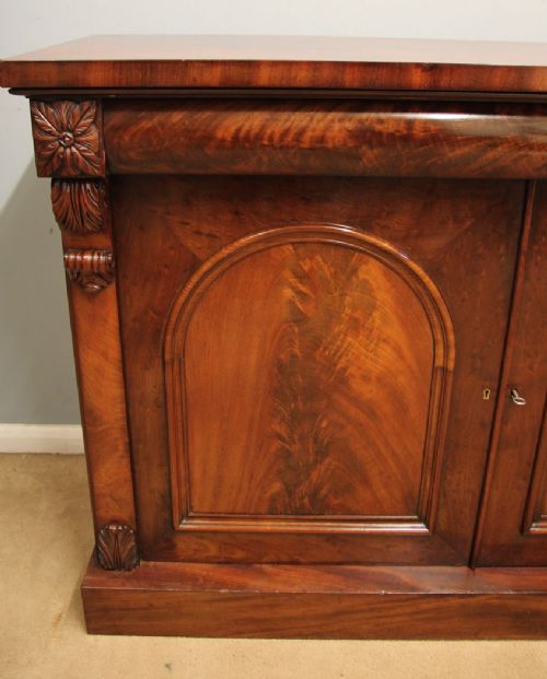 An antique Victorian flame mahogany chiffonier sideboard with two arched panel doors, carved corbels, and a plinth base. View VIII