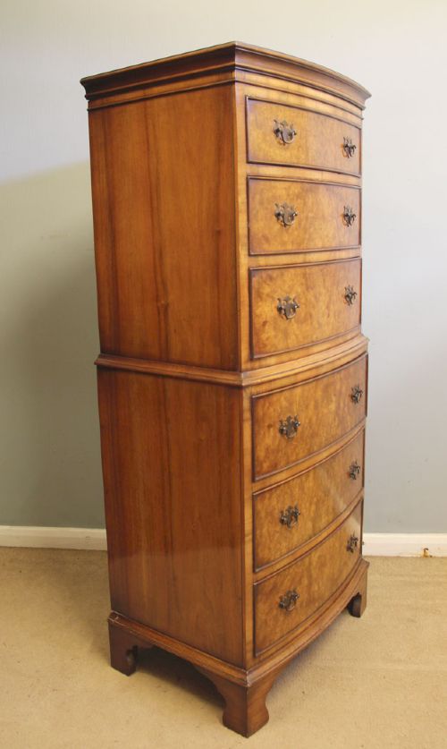 fig 1. A tall burr walnut bow-front chest on chest featuring six stacked drawers, brass handles, and bracket feet.