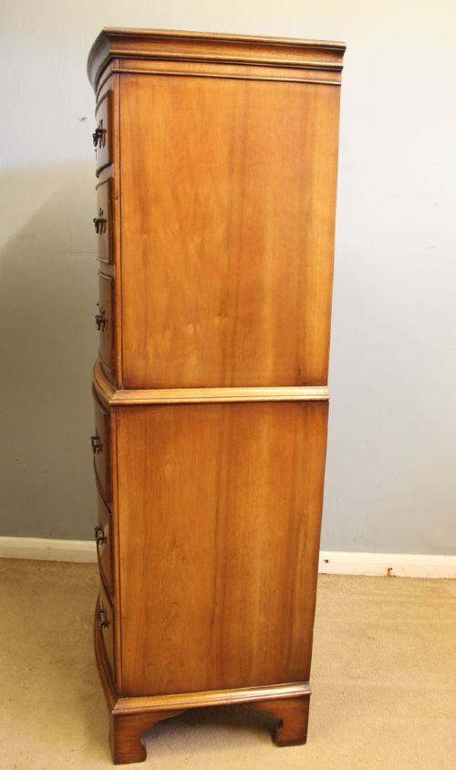 A tall burr walnut bow-front chest on chest featuring six stacked drawers, brass handles, and bracket feet. View V