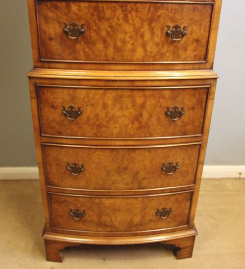 A tall burr walnut bow-front chest on chest featuring six stacked drawers, brass handles, and bracket feet. View VII