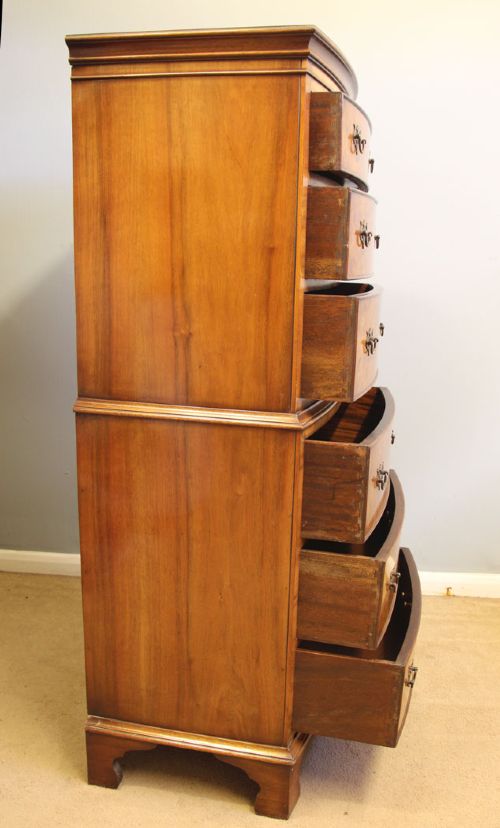 A tall burr walnut bow-front chest on chest featuring six stacked drawers, brass handles, and bracket feet. View X
