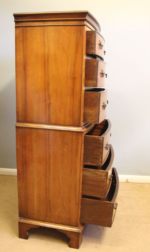 A tall burr walnut bow-front chest on chest featuring six stacked drawers, brass handles, and bracket feet. View XII