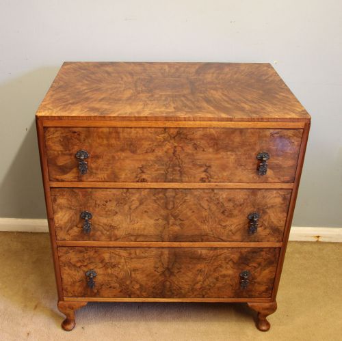fig 1. A three-drawer burr walnut chest of drawers featuring book-matched veneer patterns, ornate brass drop handles, and short cabriole legs.