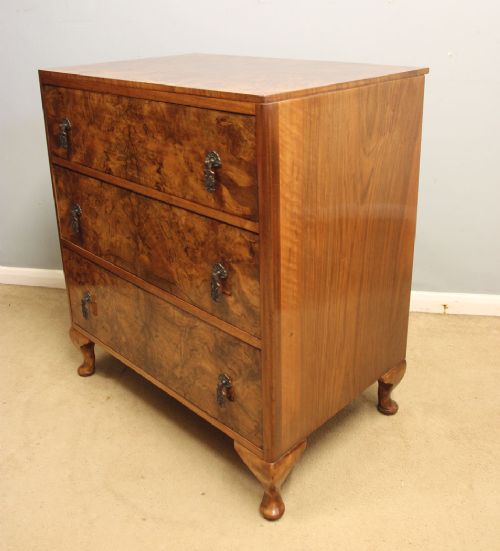 A three-drawer burr walnut chest of drawers featuring book-matched veneer patterns, ornate brass drop handles, and short cabriole legs. View IV