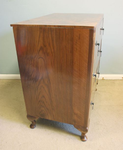 A three-drawer burr walnut chest of drawers featuring book-matched veneer patterns, ornate brass drop handles, and short cabriole legs. View V