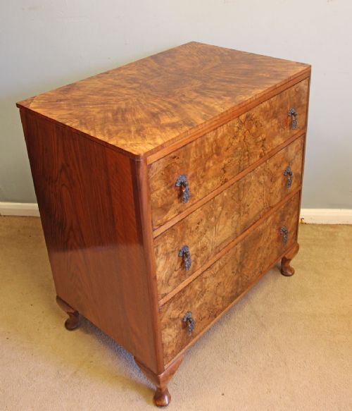 A three-drawer burr walnut chest of drawers featuring book-matched veneer patterns, ornate brass drop handles, and short cabriole legs. View X