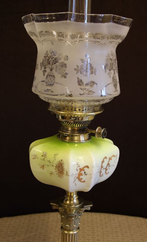 fig 1. An antique Victorian Corinthian column oil lamp featuring a brass fluted column on a stepped square base, a painted green glass reservoir, an etched shade, and a clear glass chimney.