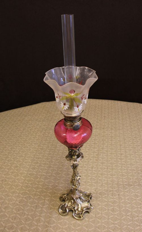fig 1. An antique Victorian peg oil lamp featuring a cast brass base, a red cranberry glass font, a painted frosted tulip glass shade, and a clear chimney.