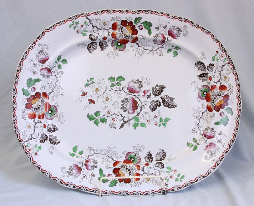 A large 19th-century oval ironstone meat dish featuring a scalloped rim, geometric border, and hand-painted polychrome floral motifs on a white background.