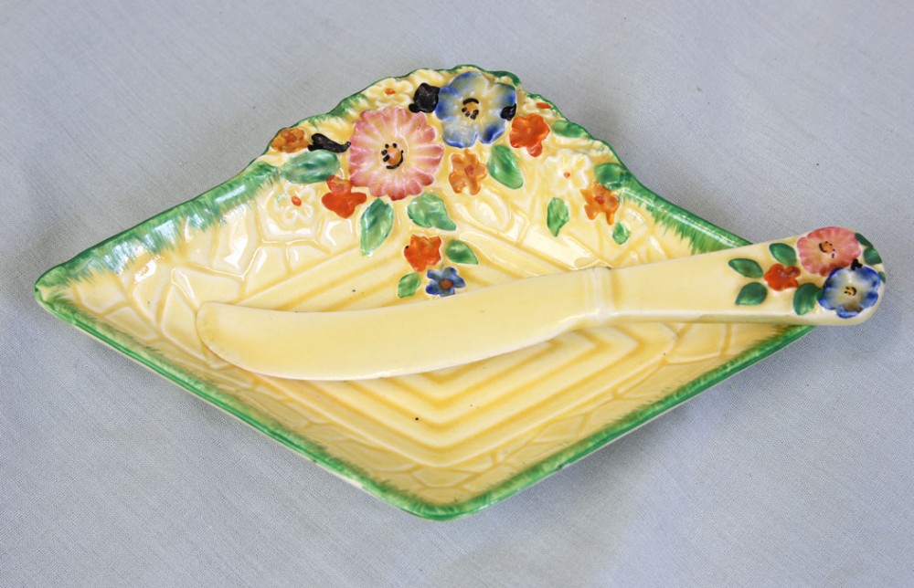 A diamond-shaped yellow glazed ceramic butter dish featuring moulded lattice pattern details, raised hand-painted flowers, and a matching ceramic butter knife.