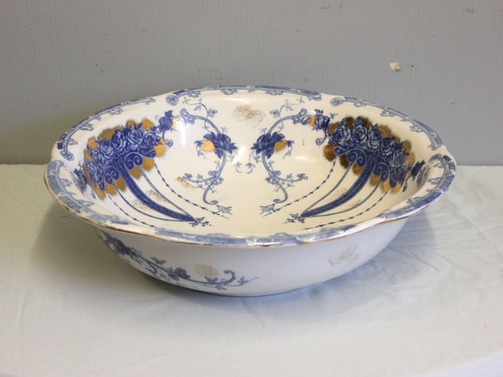 A large round antique ceramic wash bowl decorated with blue floral transferware patterns and gold gilt detailing on a white glaze.