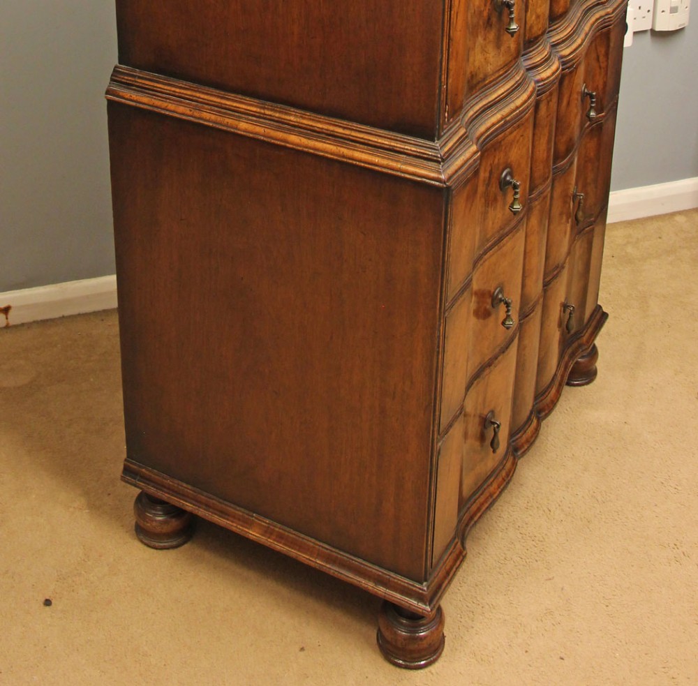 An antique figured walnut chest on chest featuring a serpentine shaped front, brass drop handles, and turned bun feet. View V