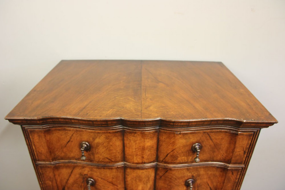 An antique figured walnut chest on chest featuring a serpentine shaped front, brass drop handles, and turned bun feet. View VII