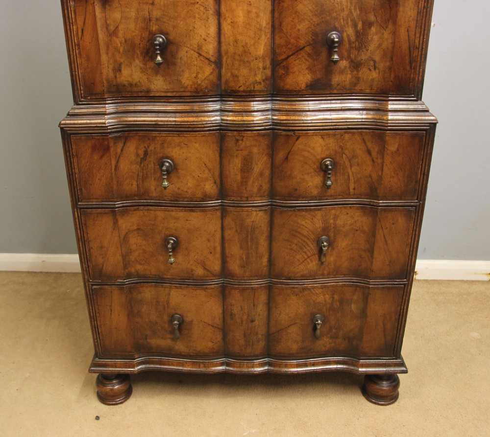 An antique figured walnut chest on chest featuring a serpentine shaped front, brass drop handles, and turned bun feet. View VIII