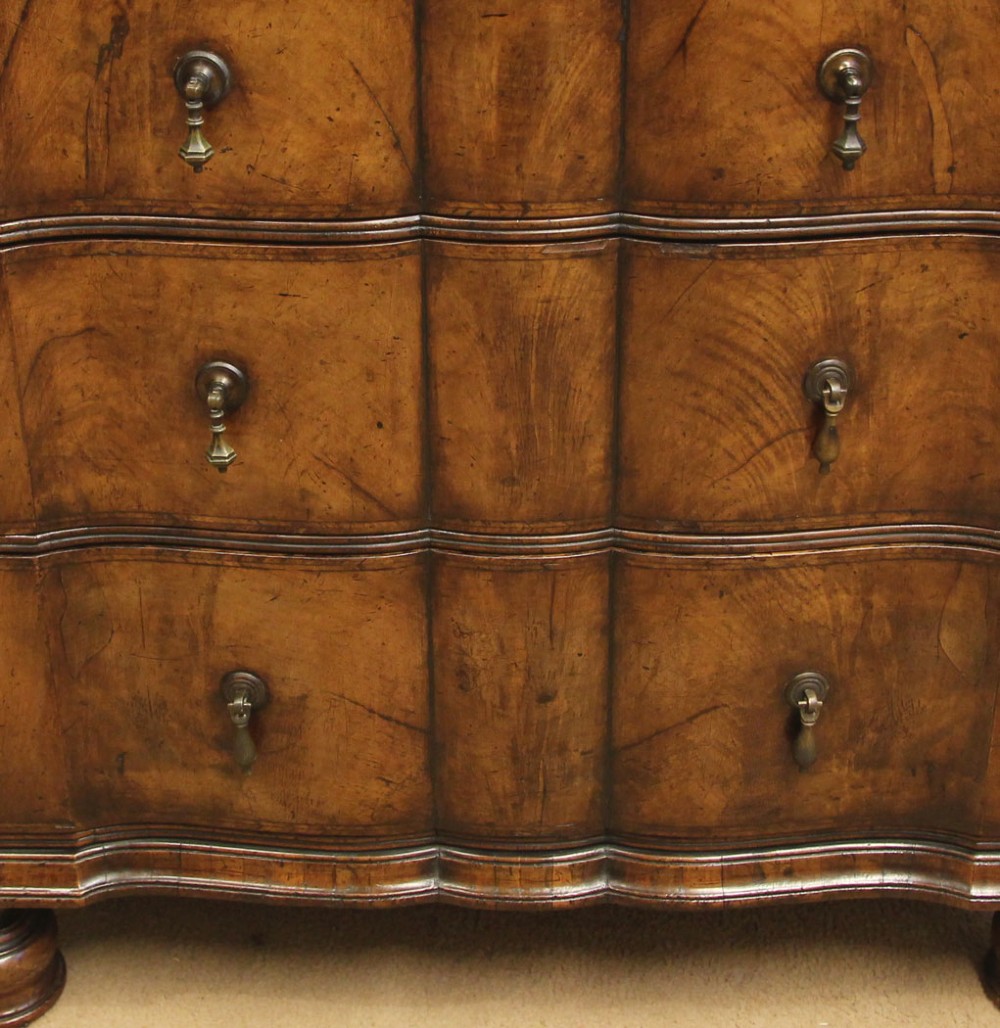 An antique figured walnut chest on chest featuring a serpentine shaped front, brass drop handles, and turned bun feet. View IX