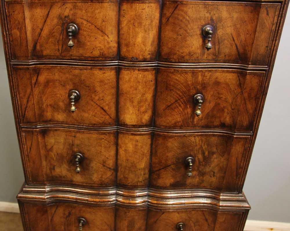 An antique figured walnut chest on chest featuring a serpentine shaped front, brass drop handles, and turned bun feet. View X