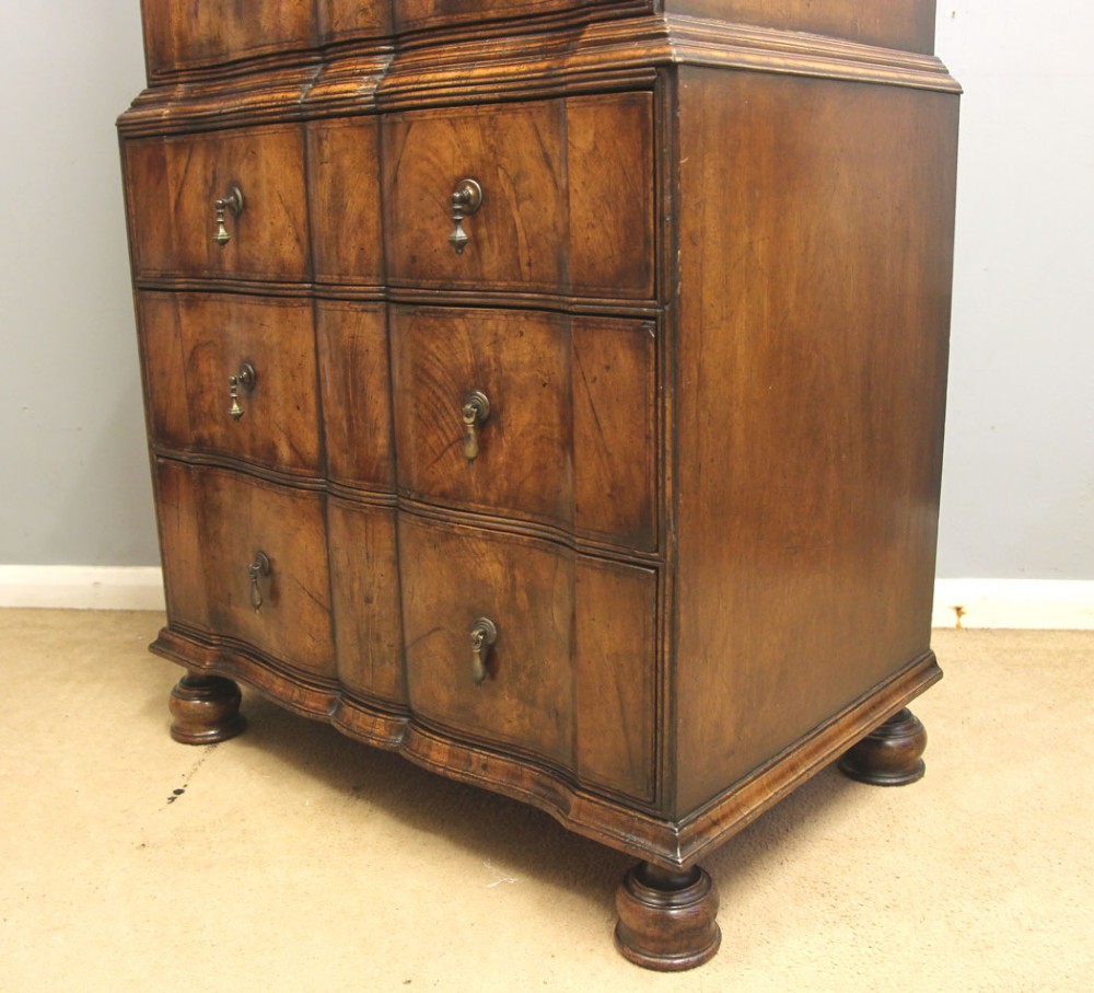 An antique figured walnut chest on chest featuring a serpentine shaped front, brass drop handles, and turned bun feet. View XIII