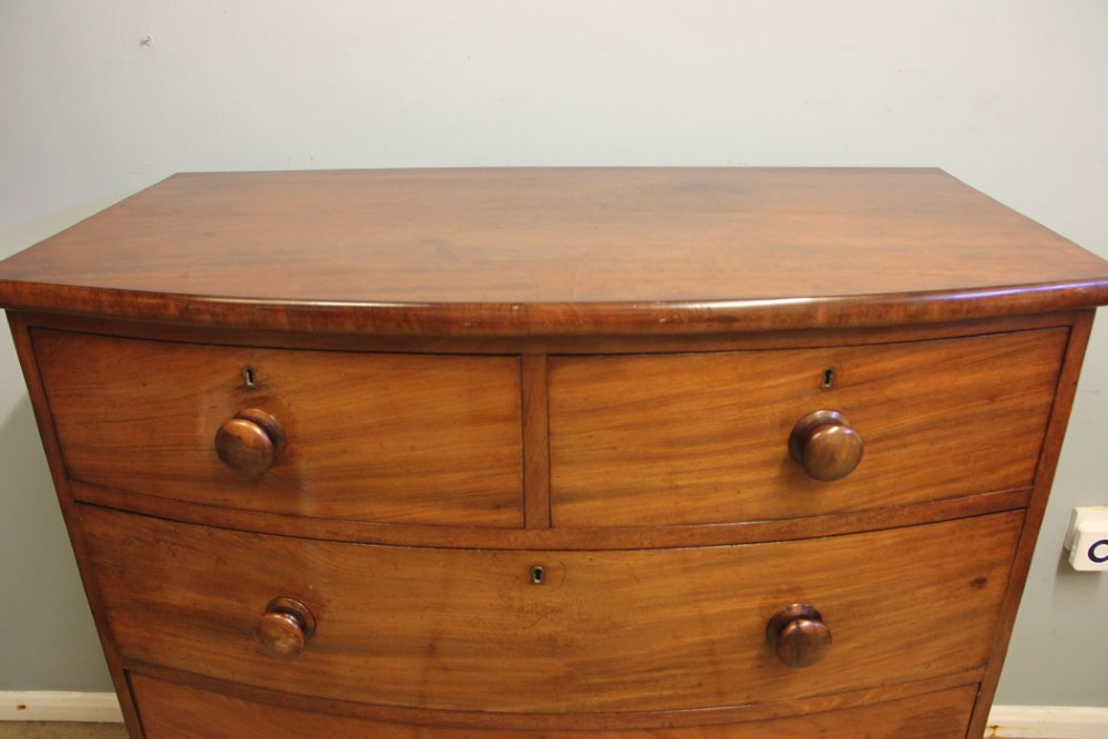A Victorian mahogany bow front chest of drawers featuring a two over three drawer layout with turned wooden handles and a curved plinth base. View V
