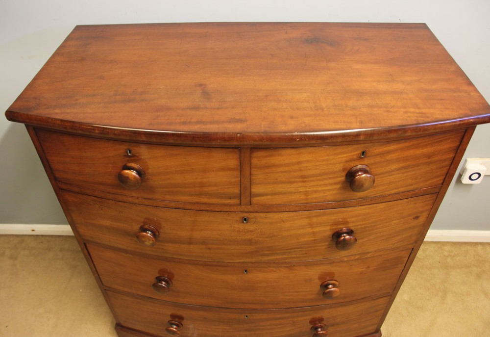 A Victorian mahogany bow front chest of drawers featuring a two over three drawer layout with turned wooden handles and a curved plinth base. View VII